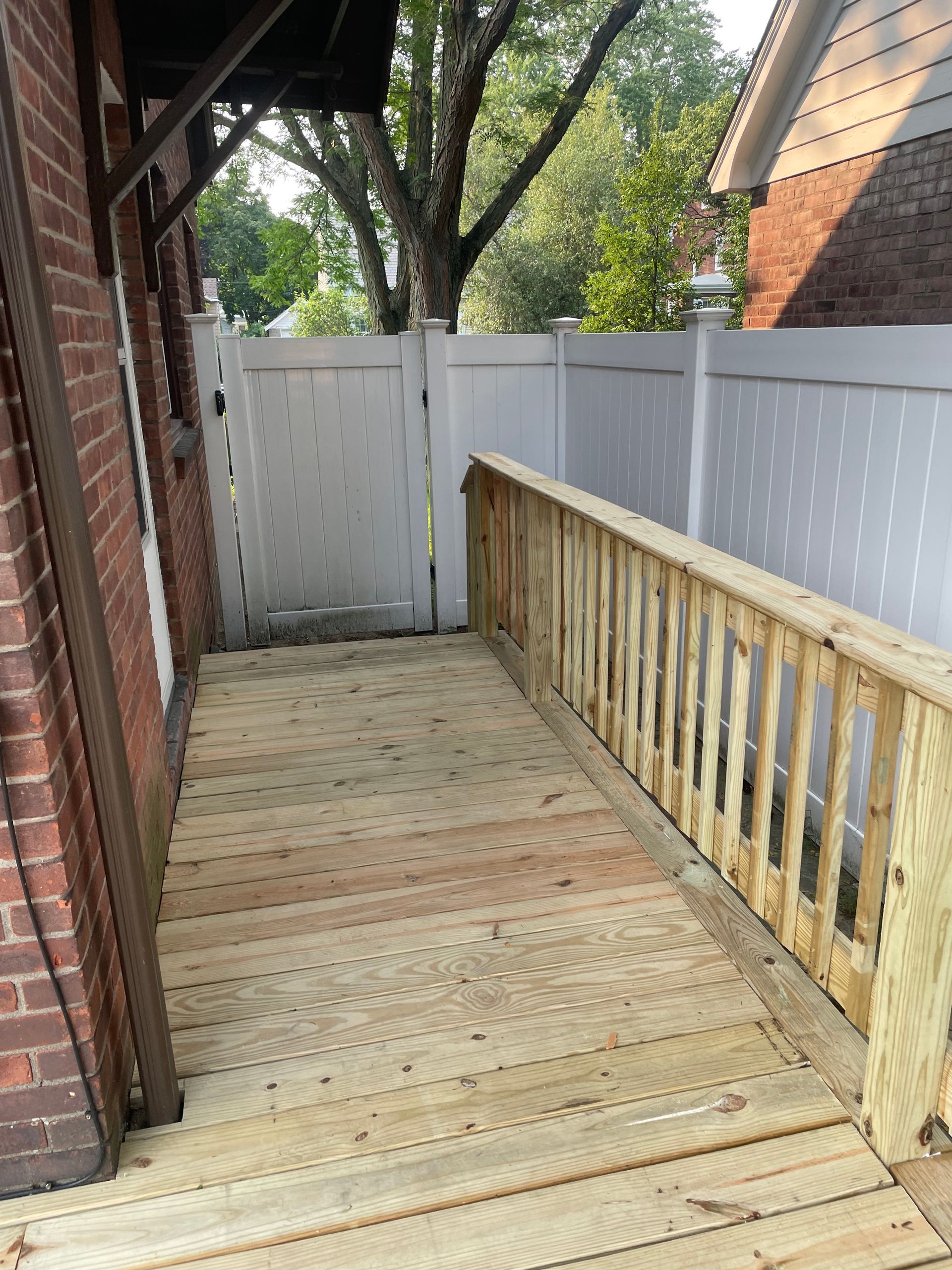 A wooden deck with a white fence and a brick building in the background.