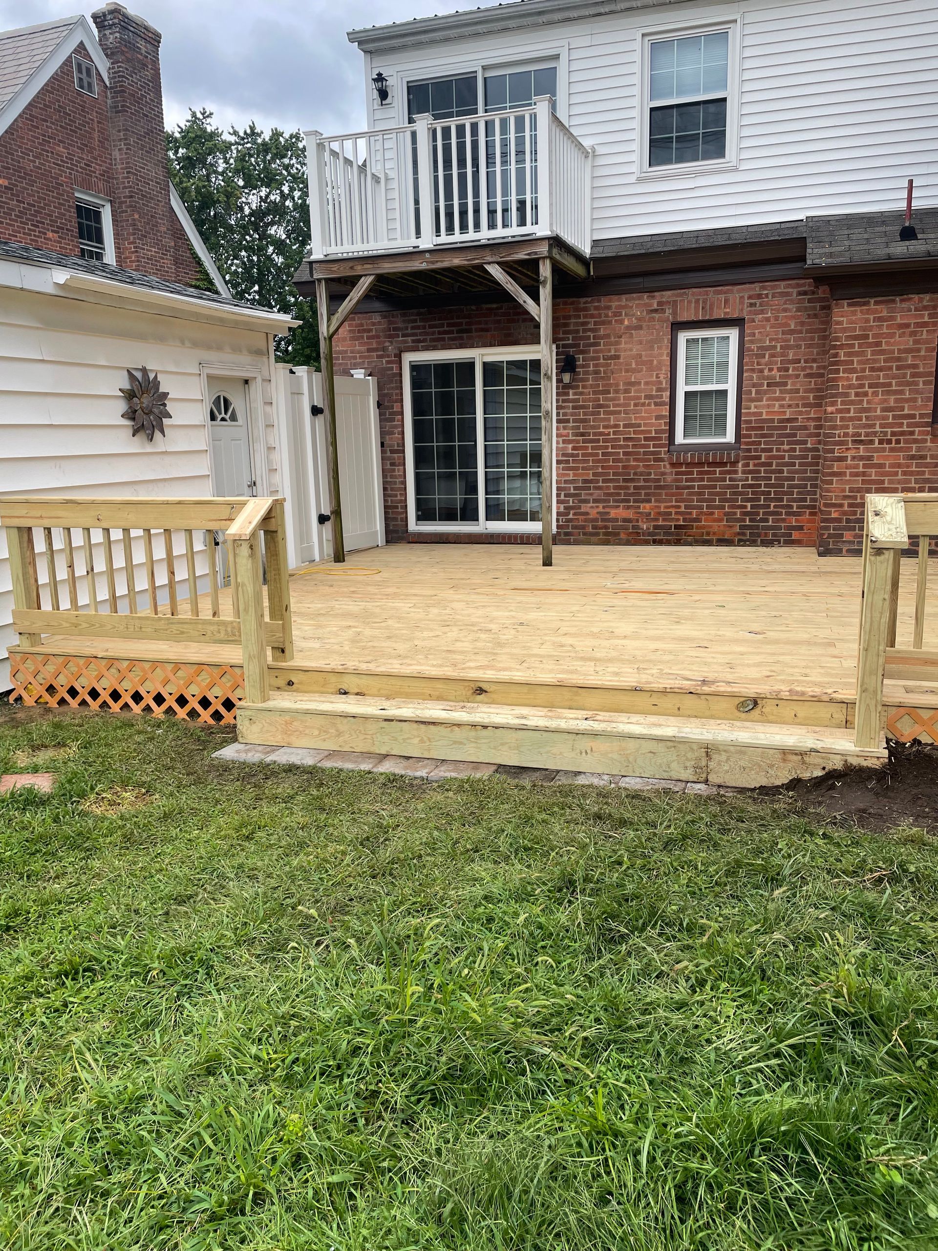 A wooden deck is sitting in front of a brick house.