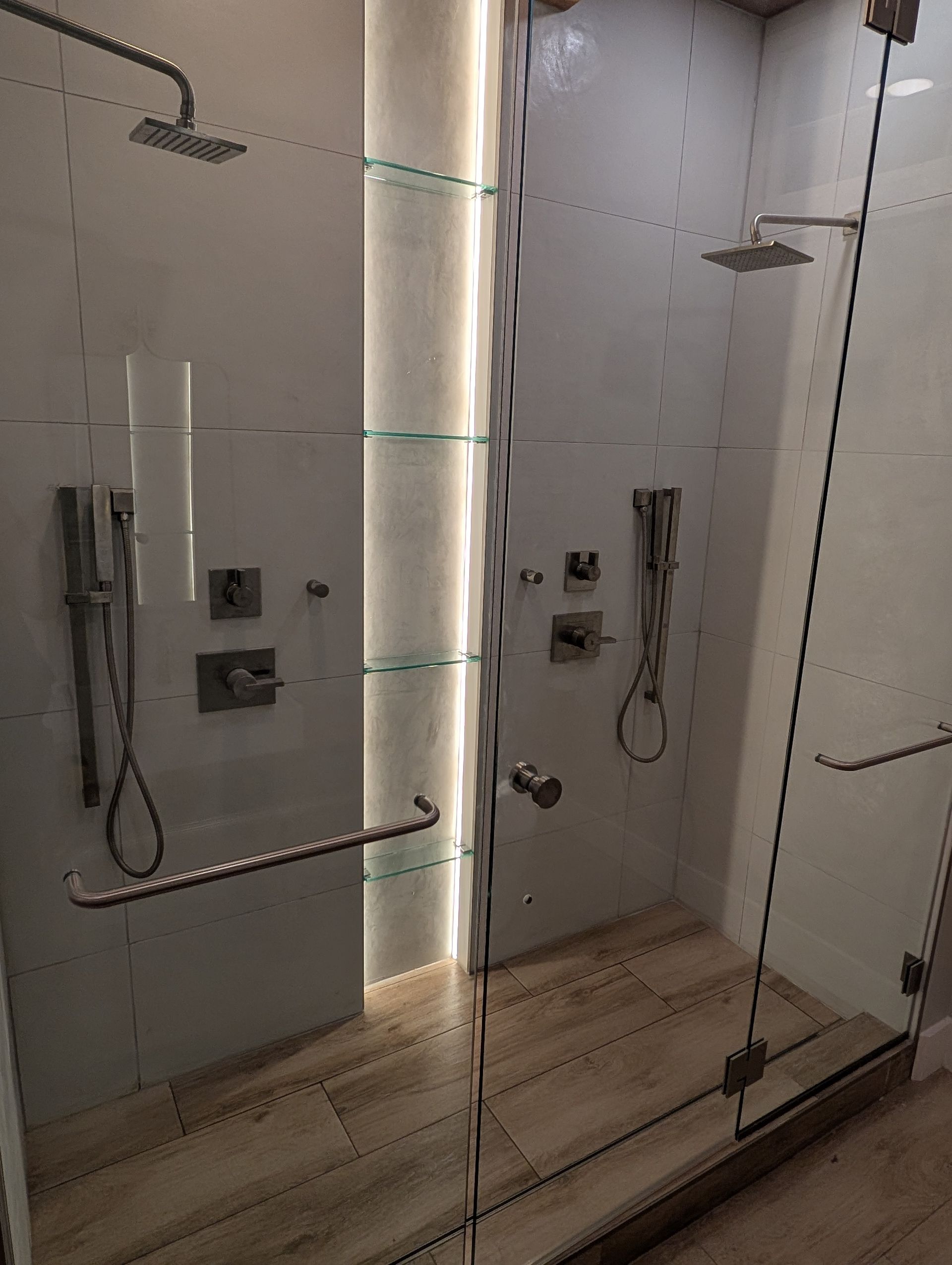 A bathroom with a walk in shower with a glass door and two shower heads.