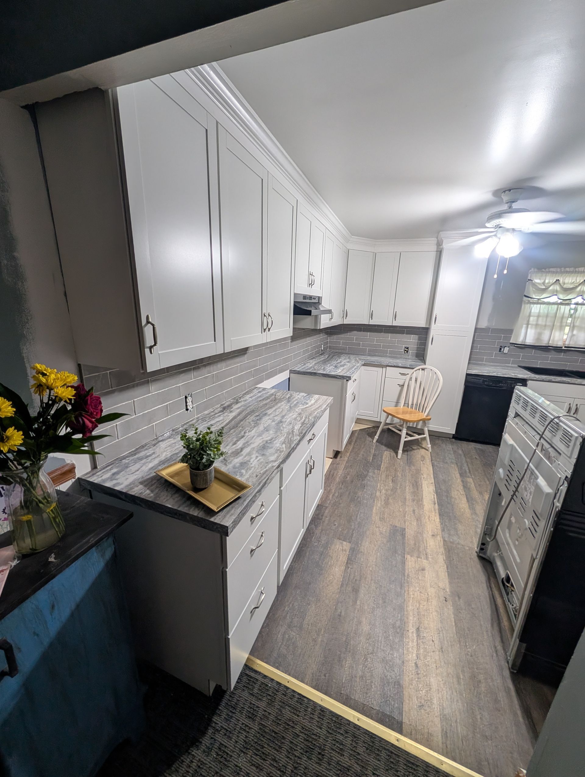A kitchen with white cabinets , granite counter tops , a stove and a chair.
