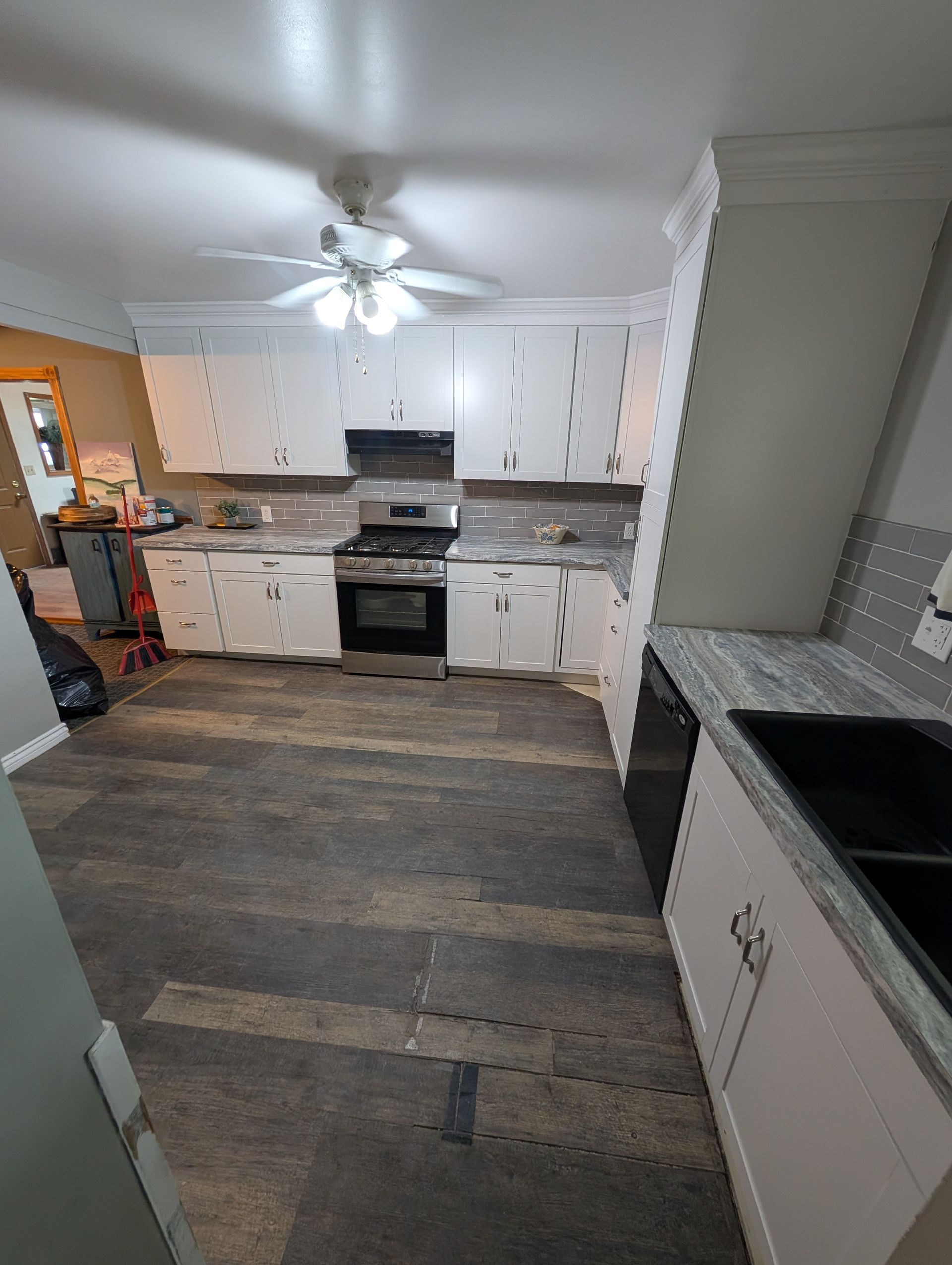 A kitchen with white cabinets , a stove , a sink , and a ceiling fan.