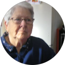 Une femme plus âgée portant des lunettes et une chemise bleue regarde la caméra.