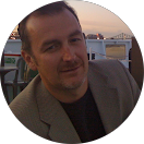 Un homme en costume et chemise noire sourit en cercle.