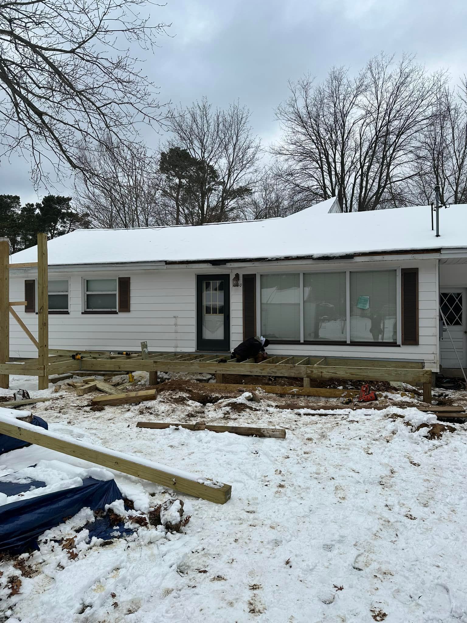 Snow-covered single-story house with damaged yard and debris in front yard