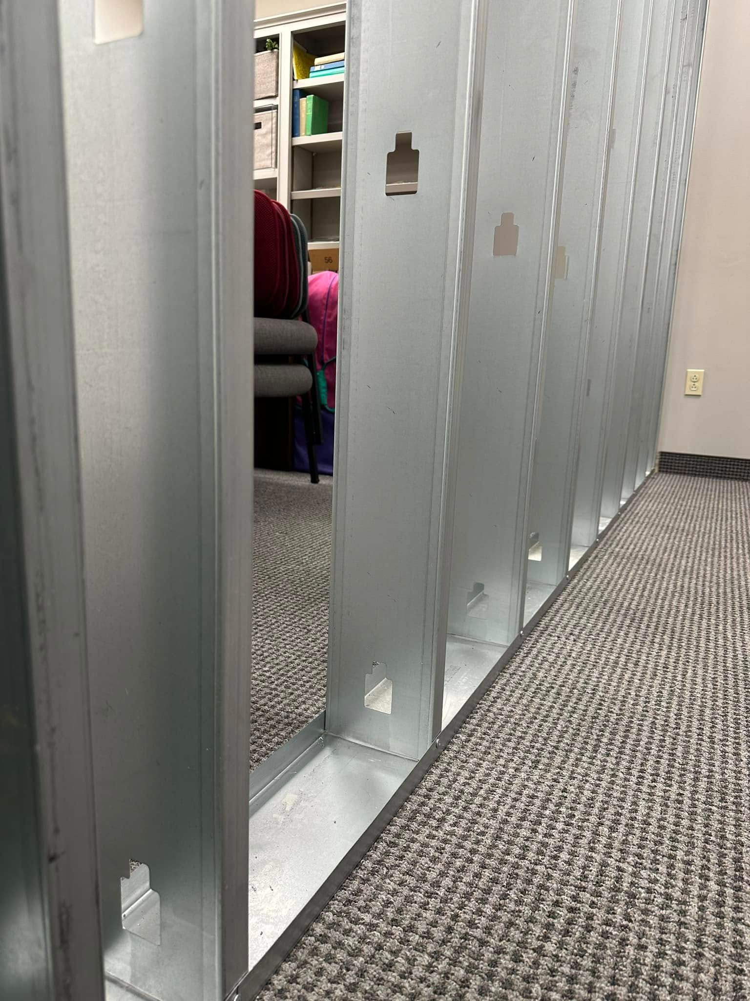 Gray metal locker row in an office hallway with a person seated in the background through an open locker door