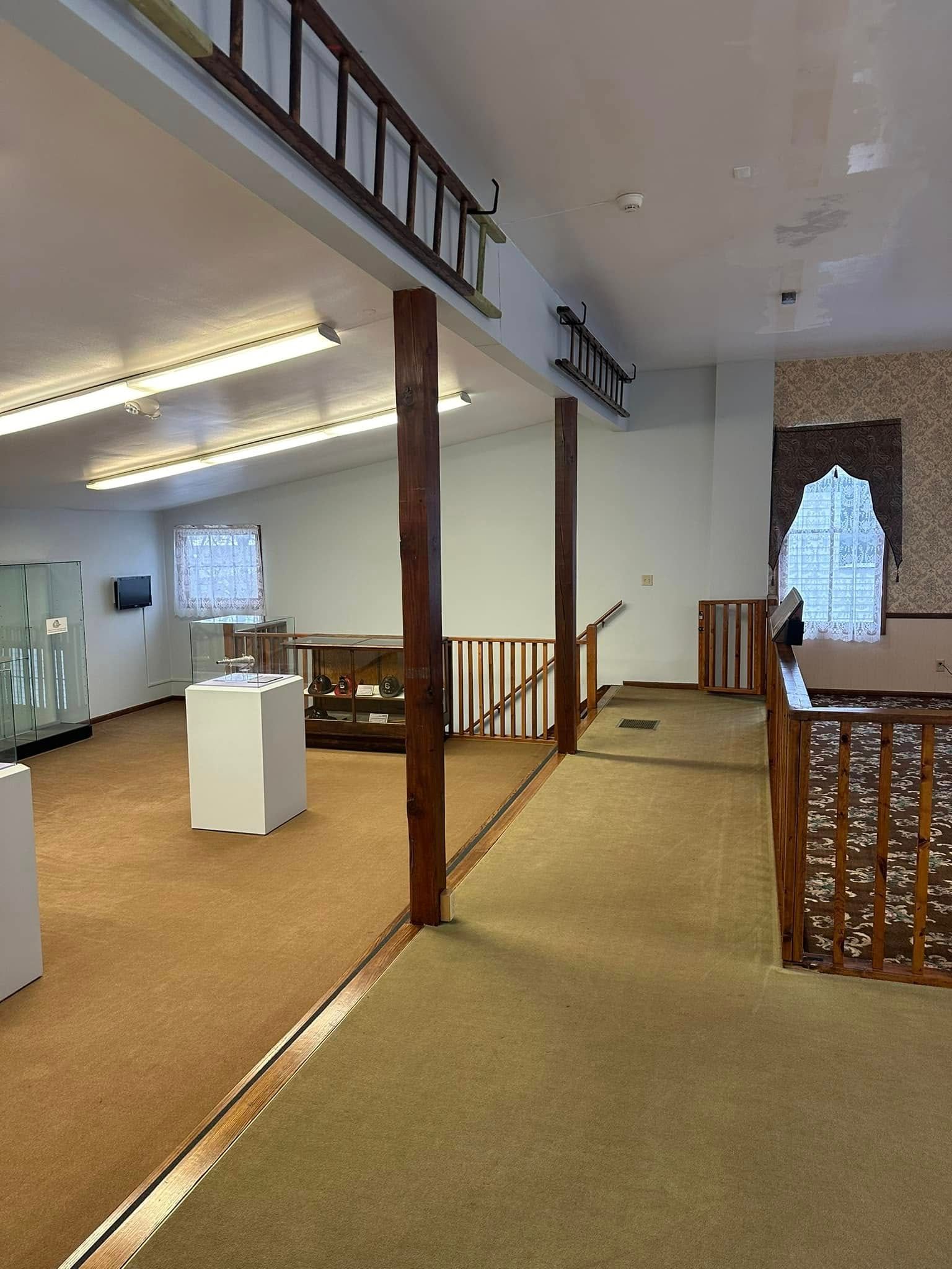 Open mezzanine hallway with beige carpet, wood posts, white walls, and a railing overlooking a lower room.
