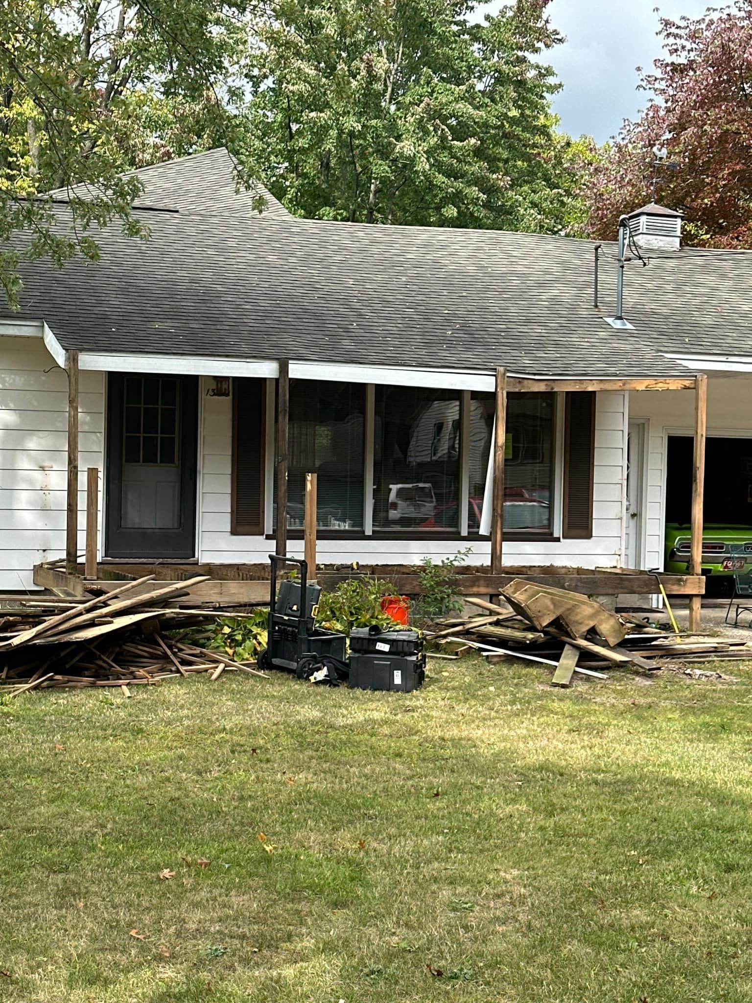 Damaged house front with sagging roof, broken porch, and scattered debris in the yard