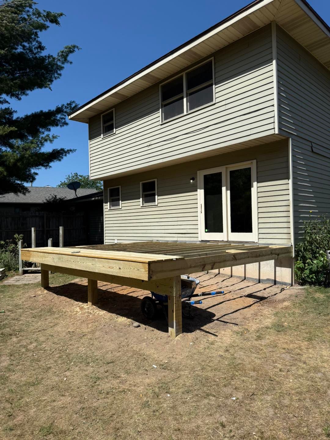 Backyard deck under construction beside a beige two-story house on a sunny day