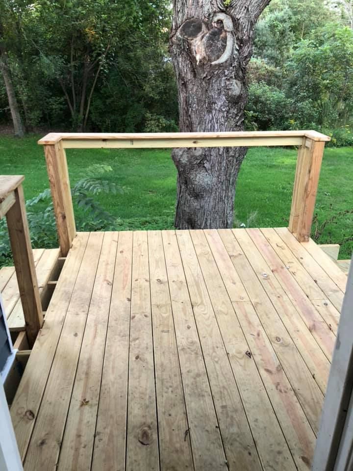 Wooden deck with simple railing overlooking a tree and green yard.