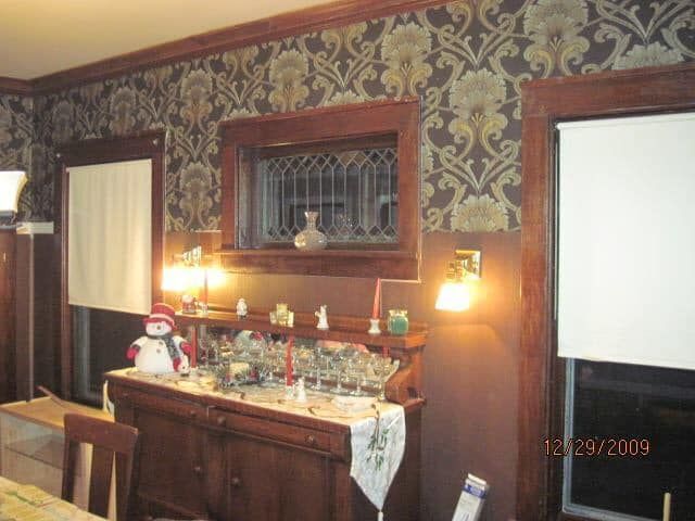 Dining room sideboard with candles, glassware, patterned wallpaper, and window shades.