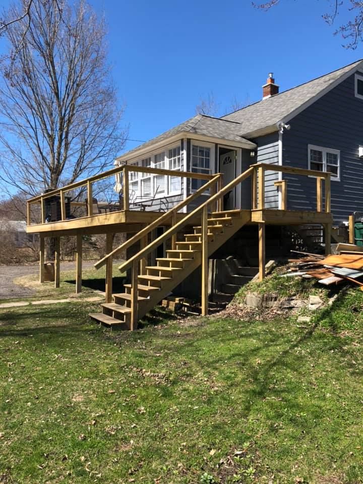Wooden backyard deck with stairs attached to a dark-sided house on a sunny day