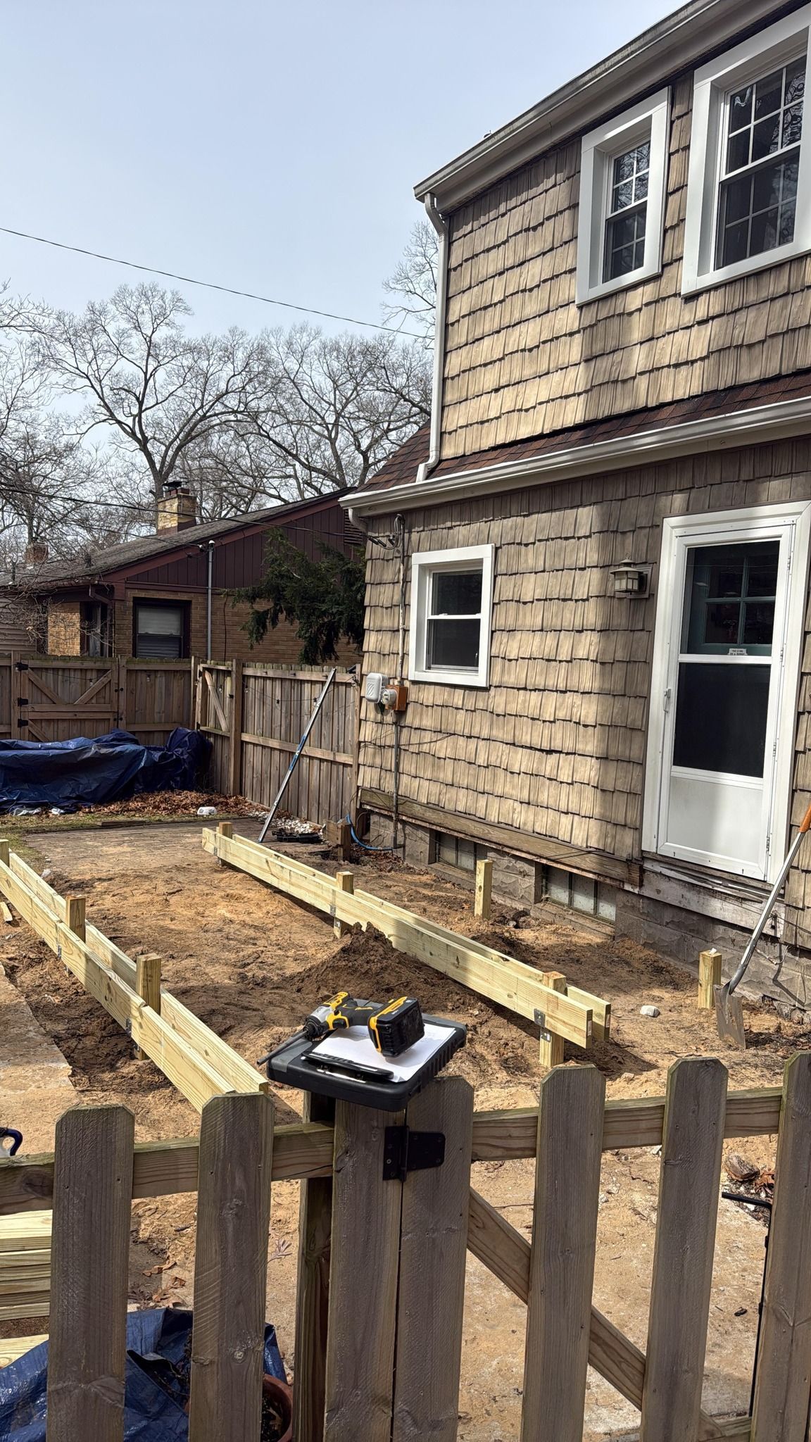 Backyard with house exterior, wooden fence, and a raised garden bed under construction