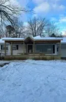 Snow-covered single-story house with a porch under a blue winter sky