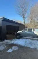 Gray pickup truck beside an open metal garage on a snowy driveway under a clear blue sky