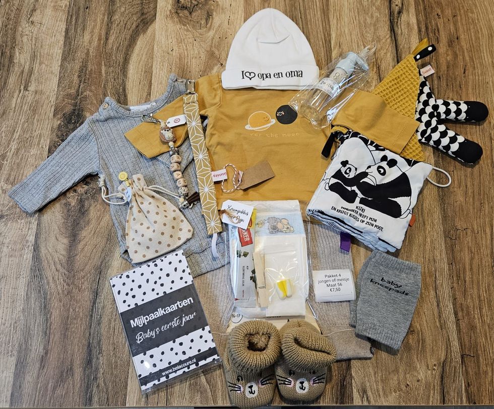 Een platte legging van babykleding en -accessoires in grijs, mosterdgeel en zwart-wit op een houten vloer.