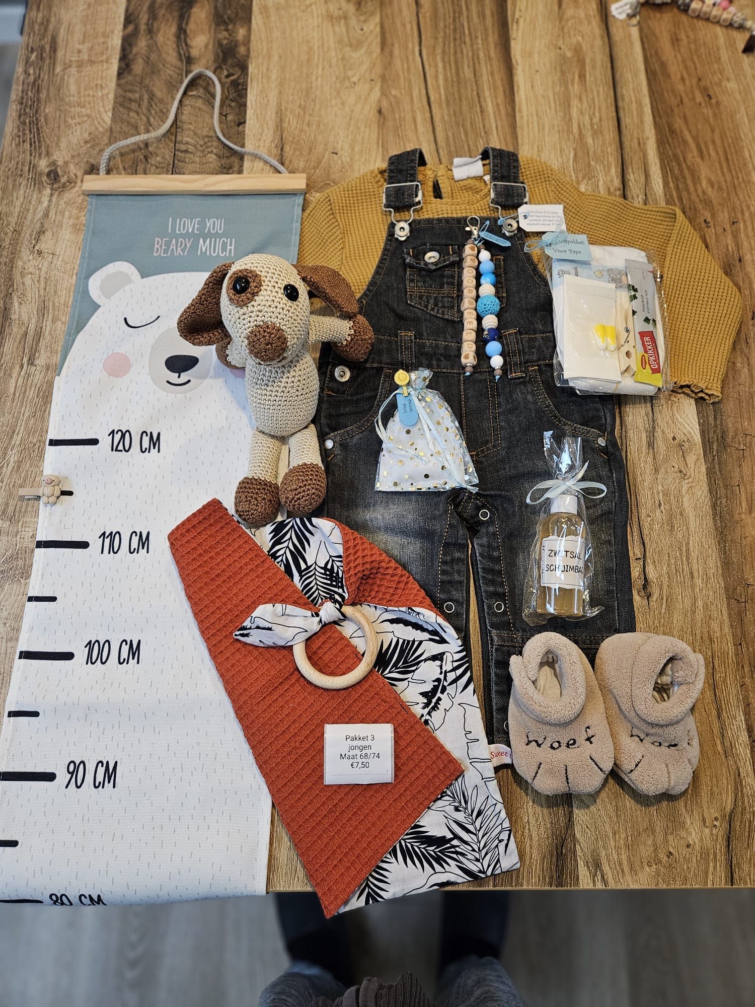 Cadeauset met hondenthema, inclusief meetlat, zwarte tas met stippen, rood etui, knuffel, ornamenten en slippers op een houten vloer.