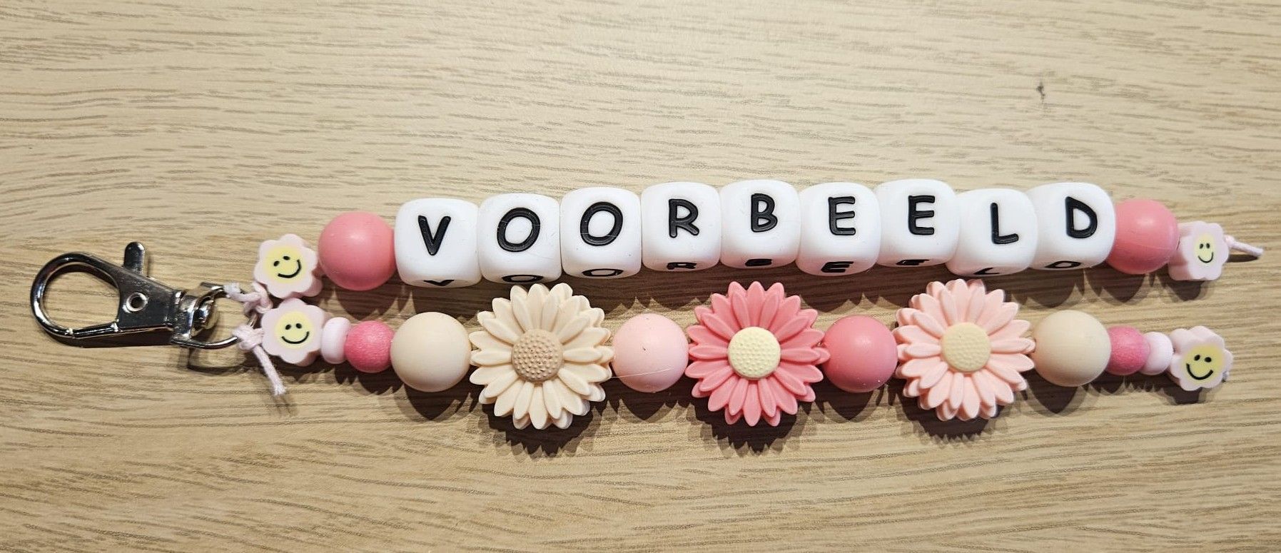 Kralenarmband met roze en witte bloemen en letterkralen die samen 