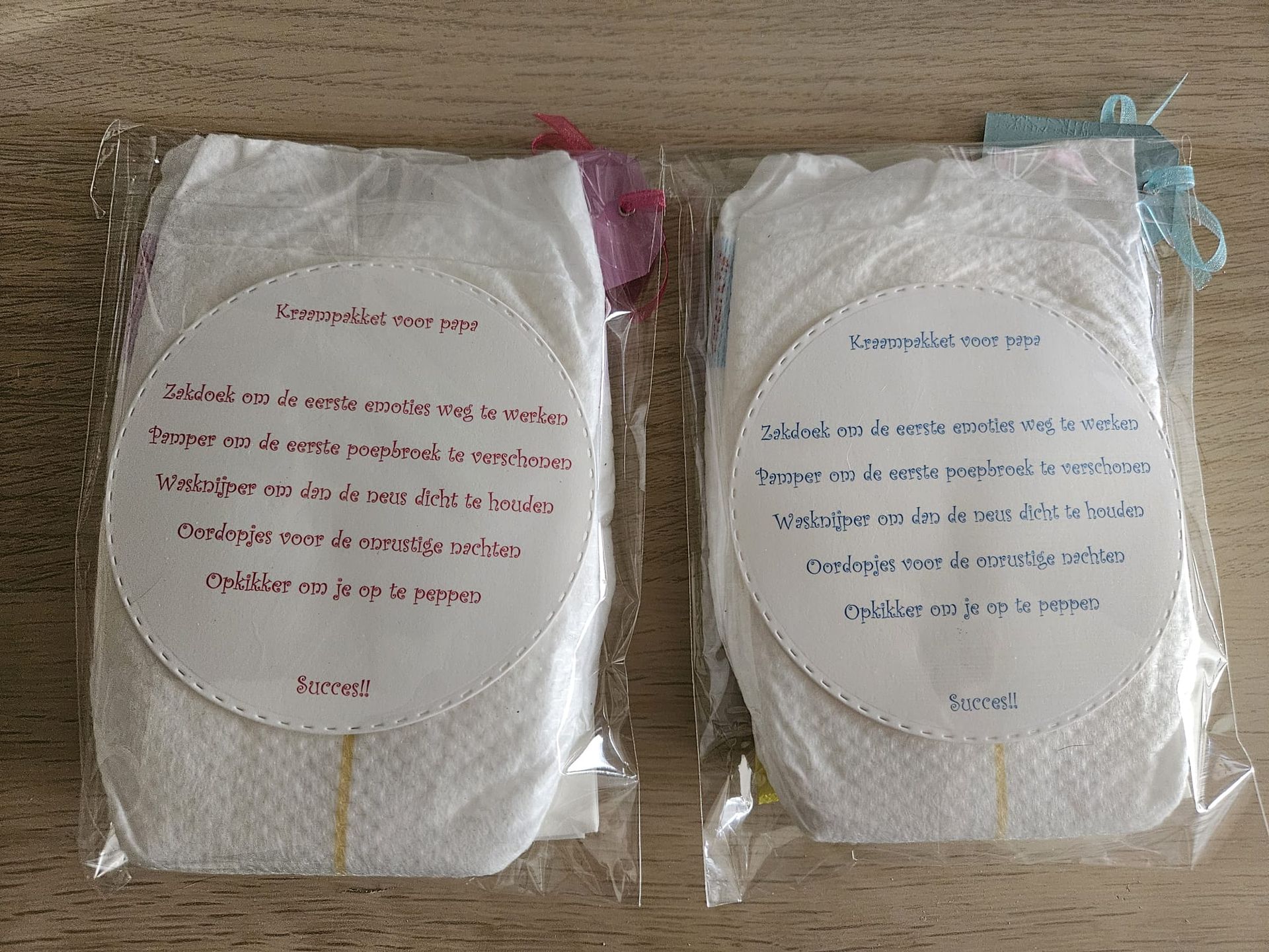 Twee ingepakte witte pakketjes met bedrukte etiketten, één met blauwe tekst en één met rode, op een houten ondergrond.