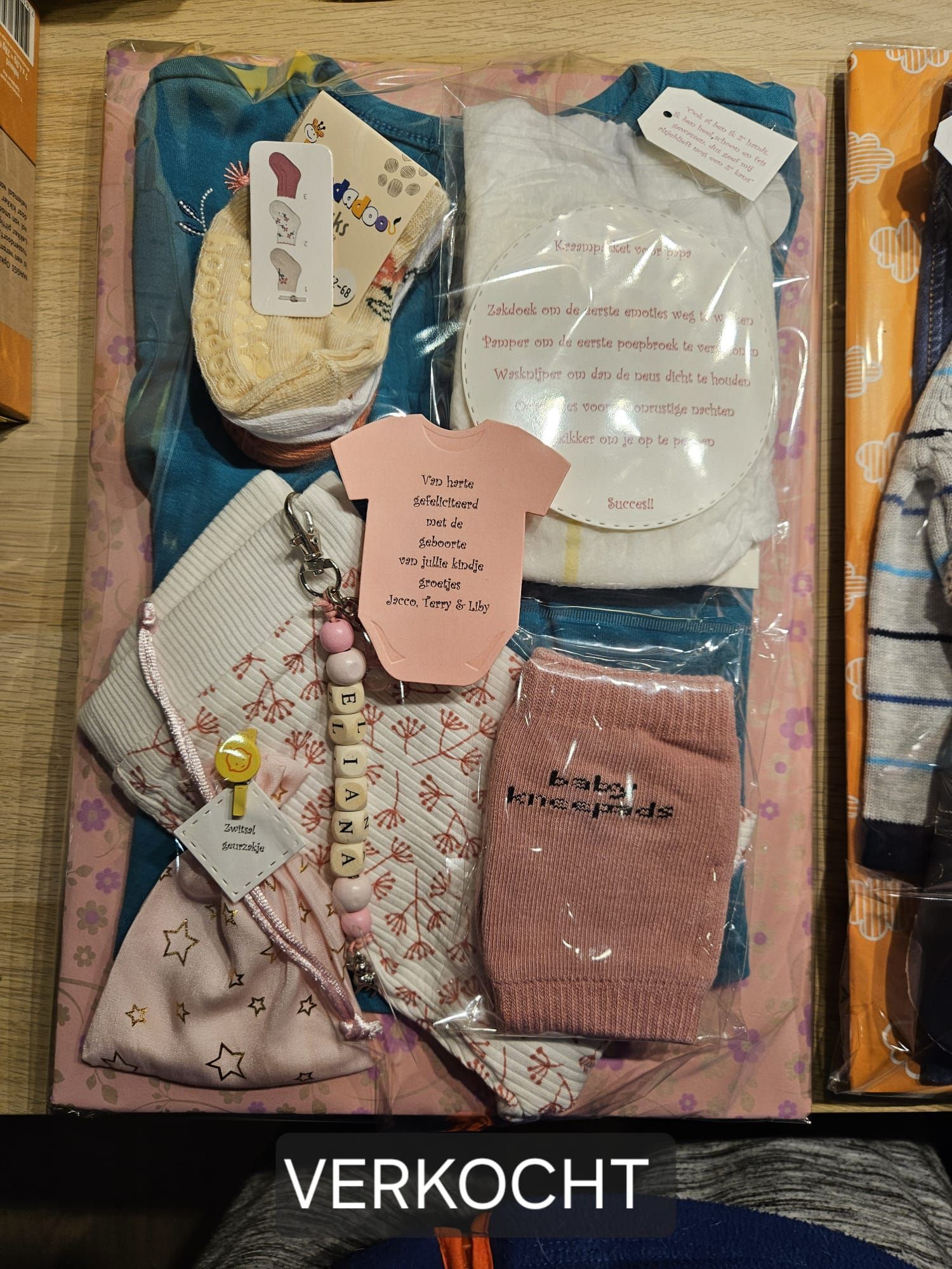 Diverse babykleding en -accessoires liggen uitgestald in een pakket, met onderaan het opschrift 
