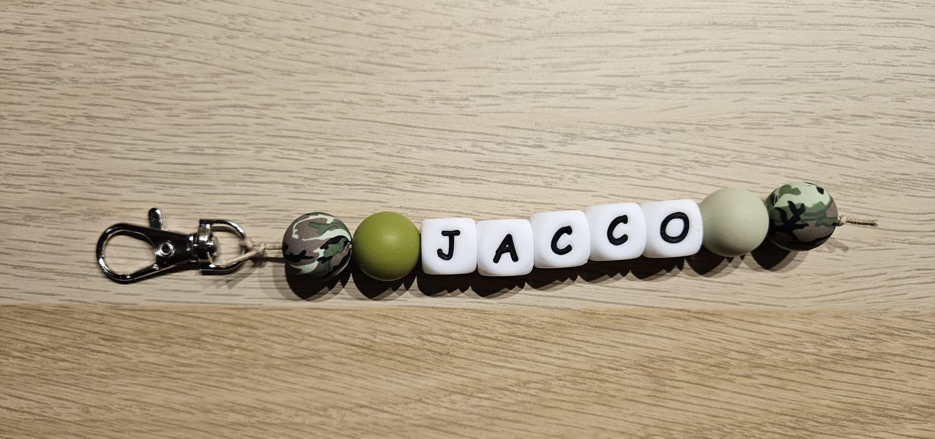 Sleutelhanger met zwarte, groene en camouflagekleurige kralen die samen het woord 