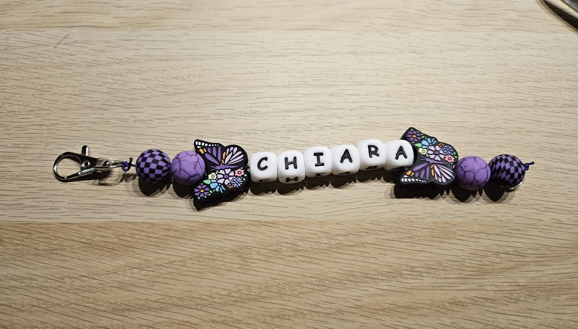 Kralen sleutelhangerarmband met paarse bedeltjes en witte letterkralen die samen 