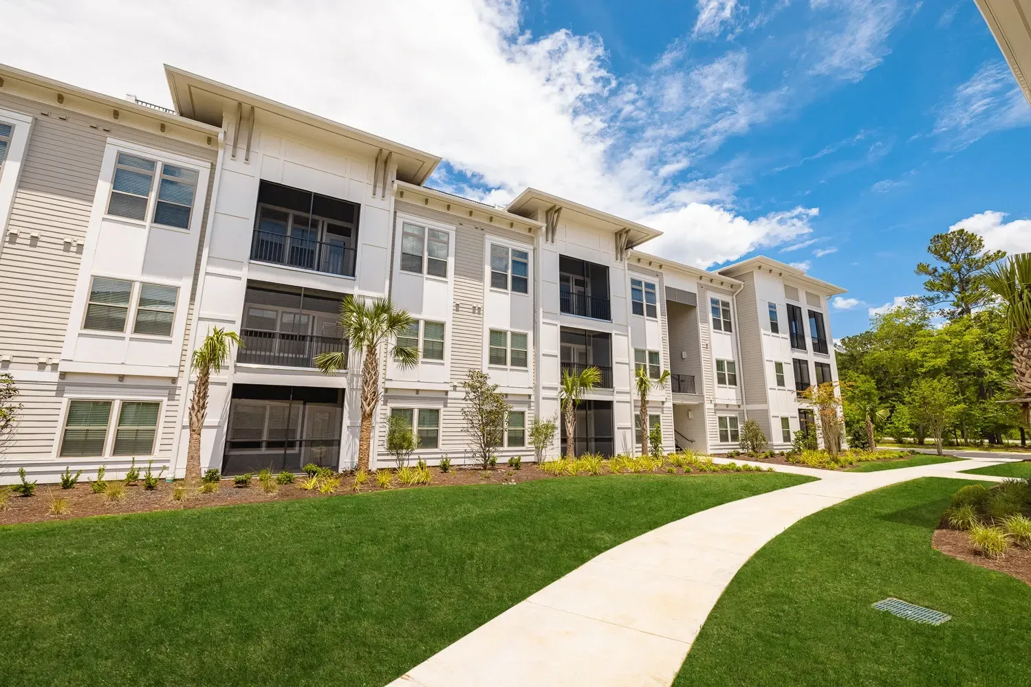 White apartment building with green lawn and curved sidewalk under a blue sky at Azure Carnes Crossing