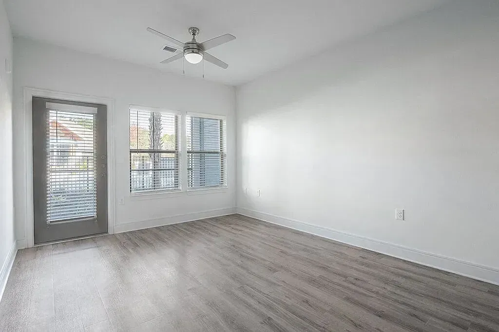 Empty modern bedroom with gray wood floors, white walls, windows, and a ceiling fan at Azure Carnes Crossing in Summerville