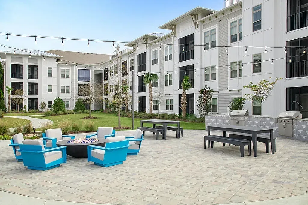 Modern apartment courtyard with blue lounge chairs, tables, and white buildings surrounding a paved patio at Azure Carnes