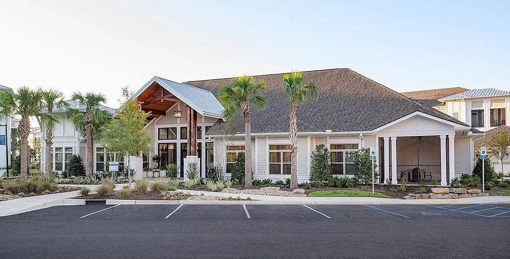 Single-story house with a thatched roof and palm trees in front, viewed from a parking lot at Azure Carnes Crossing