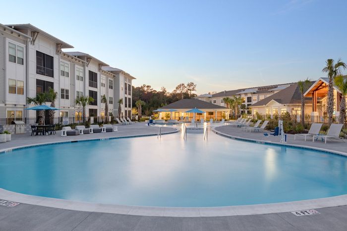 Modern apartment courtyard with blue lounge chairs, tables, and landscaped seating areas at Azure Carnes Crossing