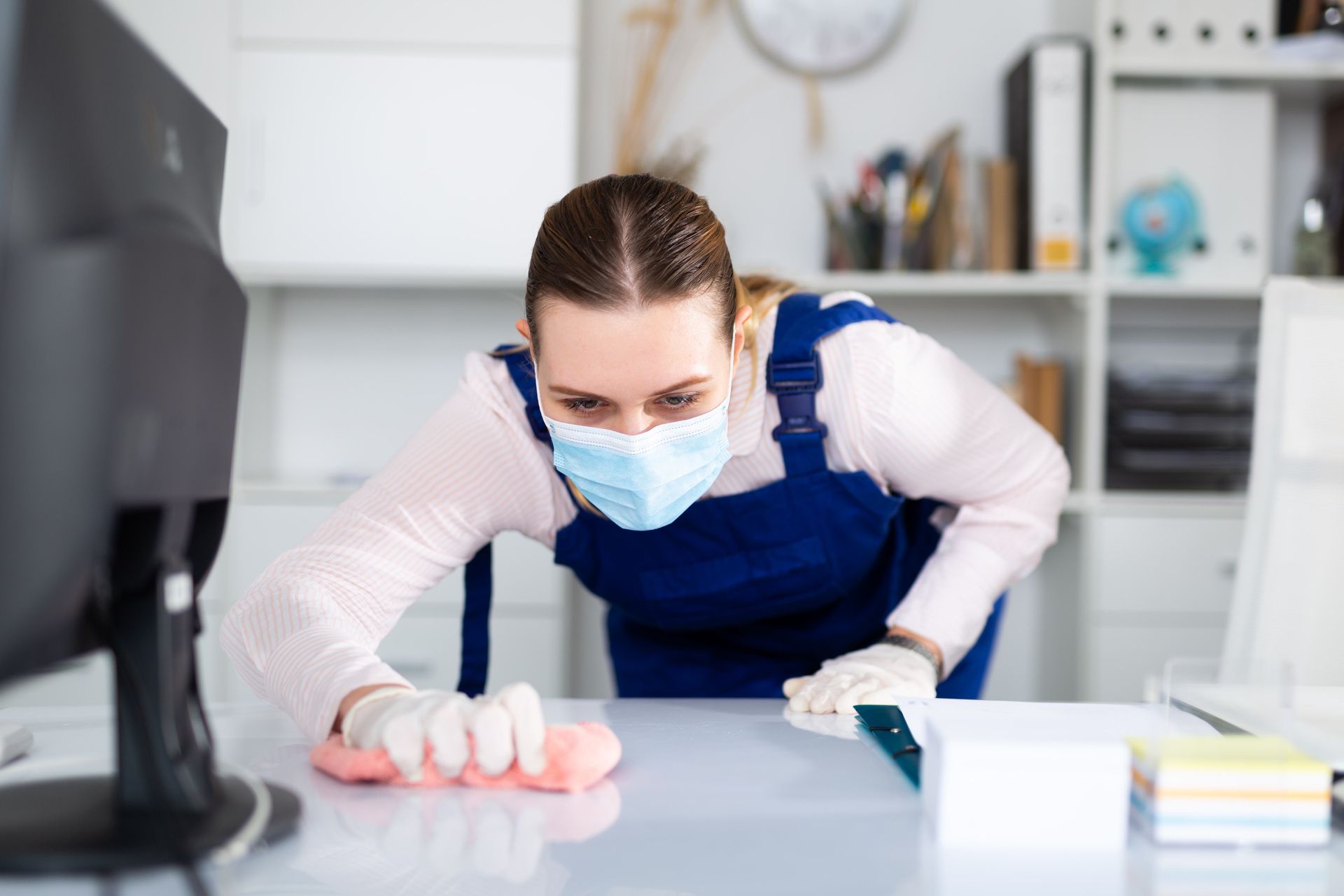 a woman wearing a mask is cleaning a desk in an office