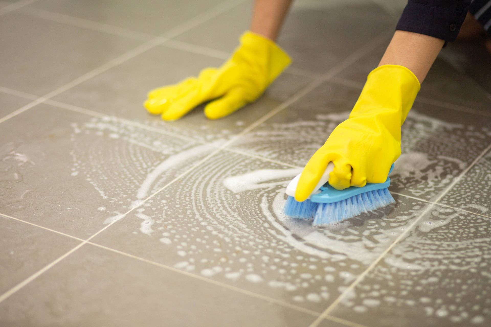 a person wearing yellow gloves is cleaning a tile floor with a brush