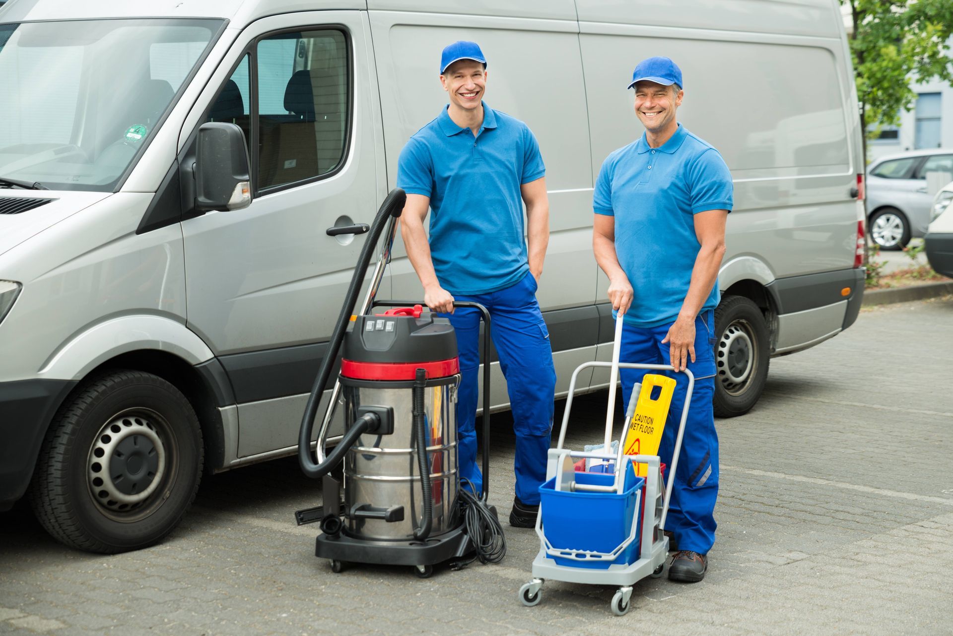 two men are standing in front of a van with cleaning equipment .