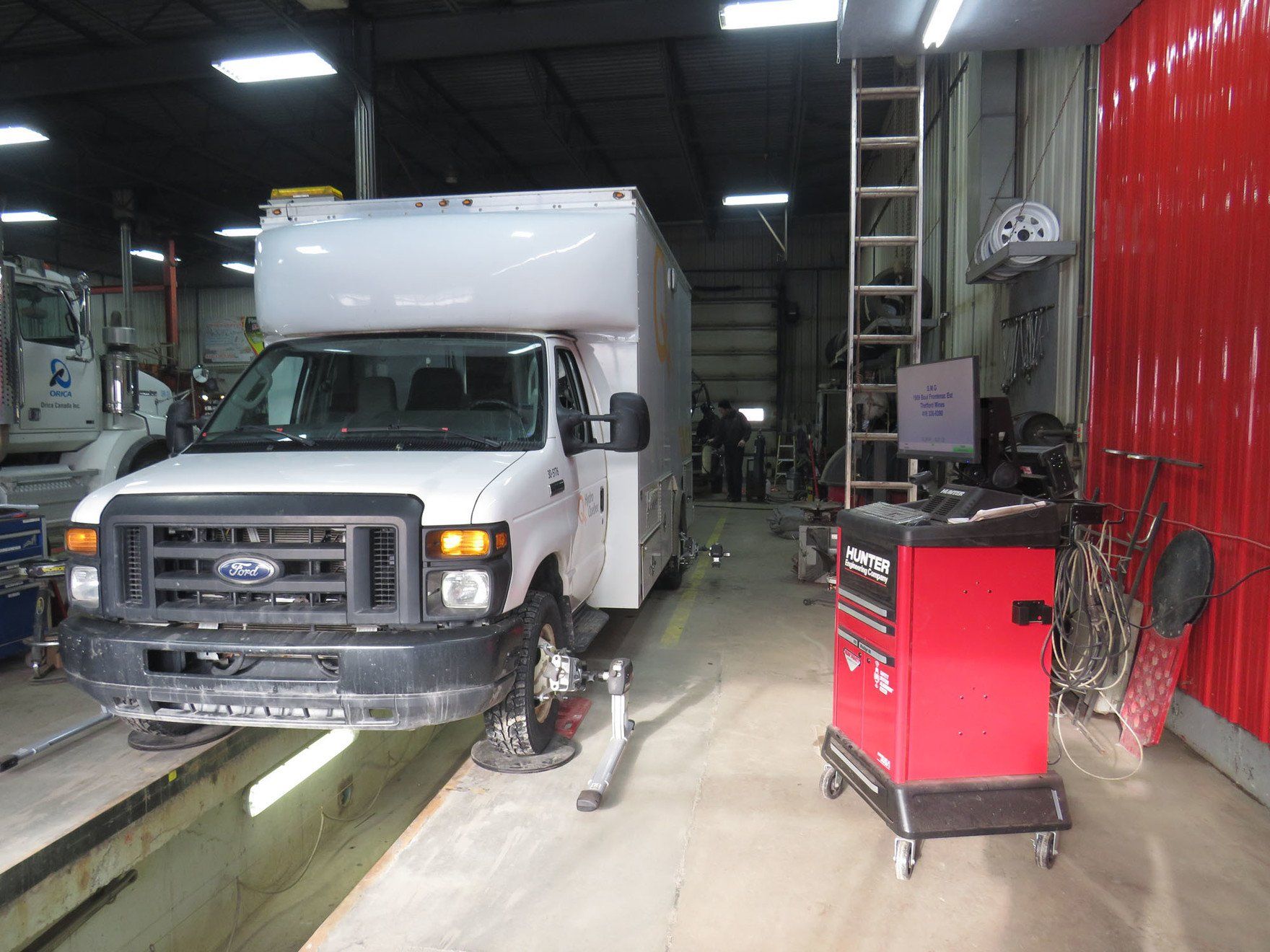 Fourgonnette blanche sur un pont élévateur dans un garage. Armoire à outils rouge à proximité.