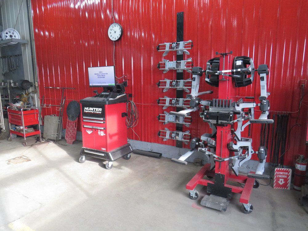 Machine d'alignement de voiture rouge dans un garage, à côté d'un coffre à outils, avec un mur rouge.