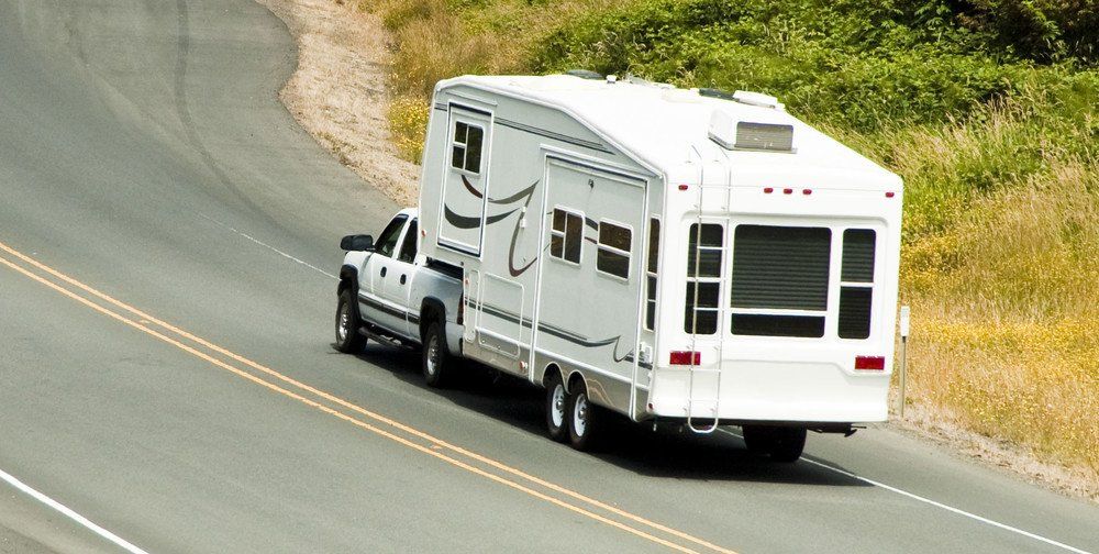 Une camionnette blanche tractant un gros camping-car sur une route sinueuse, traversant une zone herbeuse.
