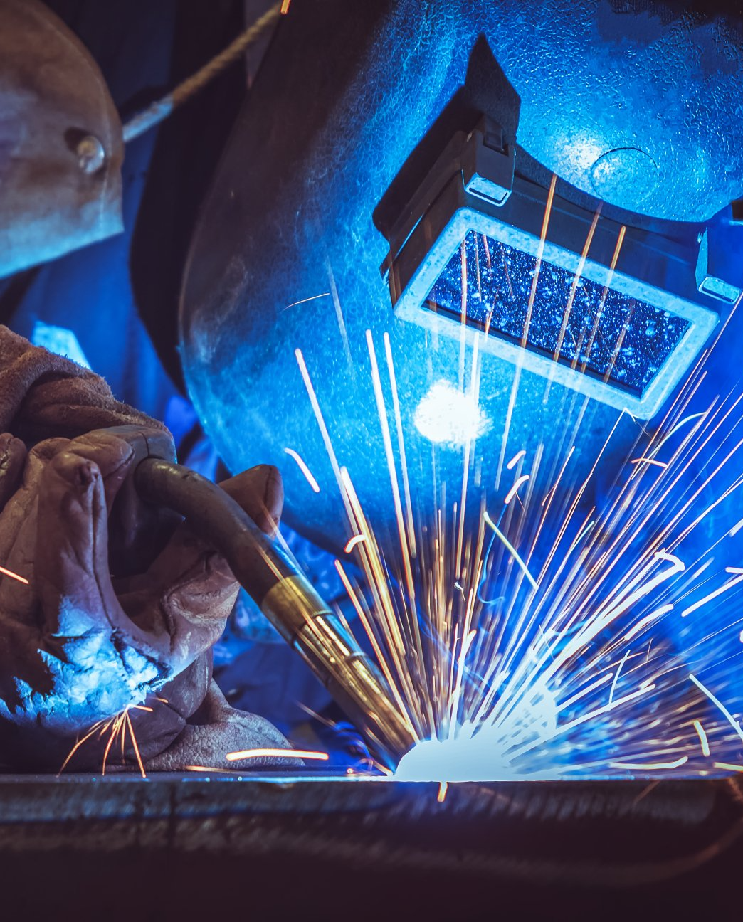 Soudeur sous lumière bleue portant un équipement de protection, des étincelles jaillissant de la torche de soudage.