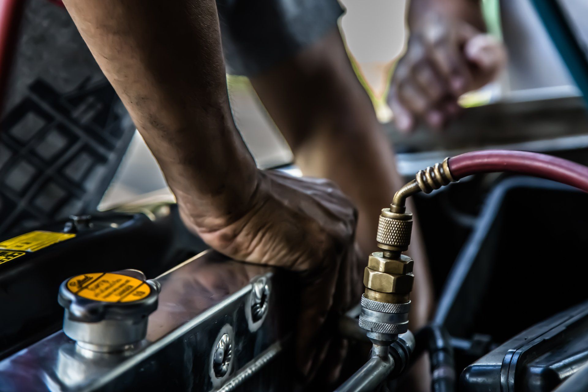Un mécanicien travaille sur un moteur de voiture et raccorde un tuyau. Ses mains sont visibles.
