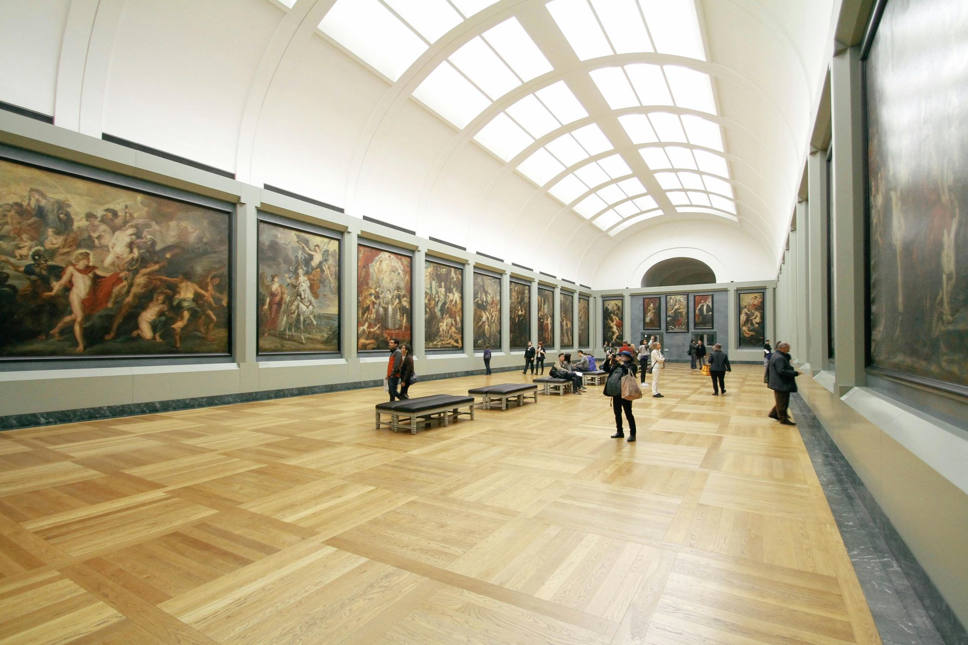 A group of people are walking through a museum filled with paintings.