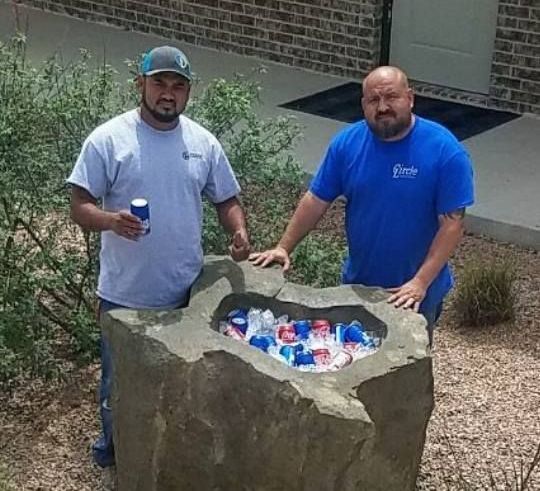 Two men standing next to a large rock filled with soda cans