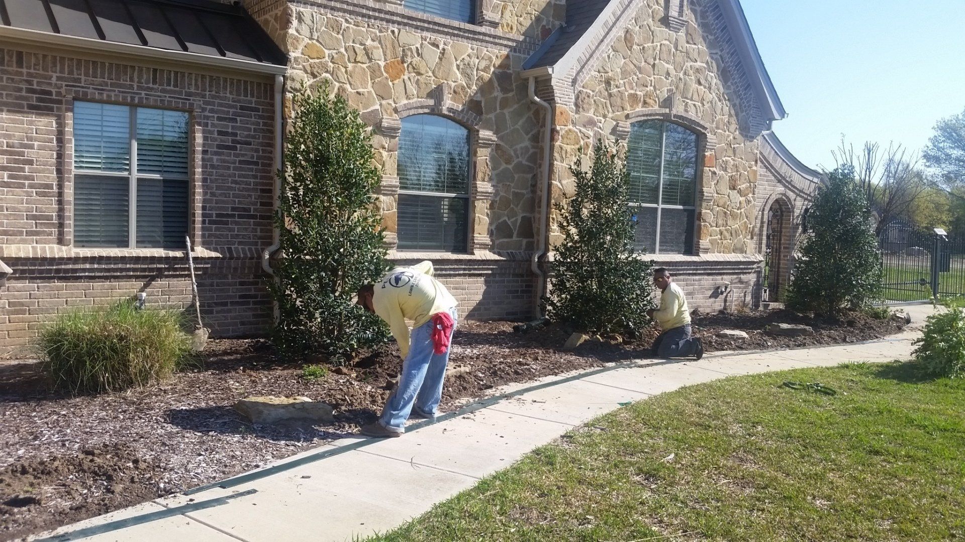 Two men are working on a sidewalk in front of a stone house