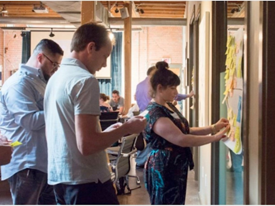 A group of people are writing on sticky notes on a wall.