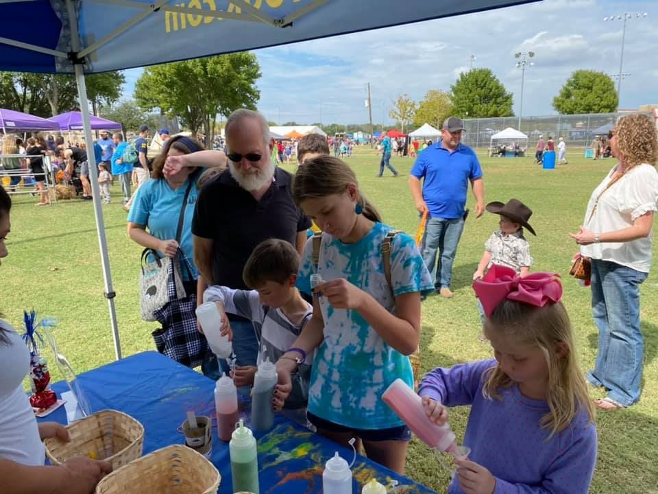 A group of children are sitting at a table with bottles of paint.