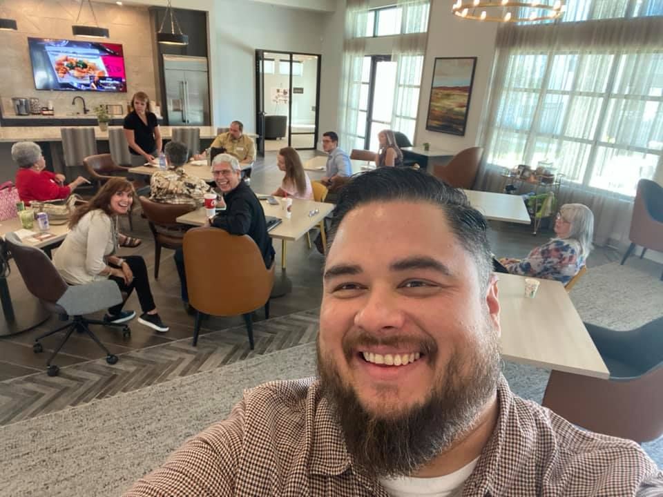 A man is taking a selfie in a restaurant with a group of people sitting at tables.