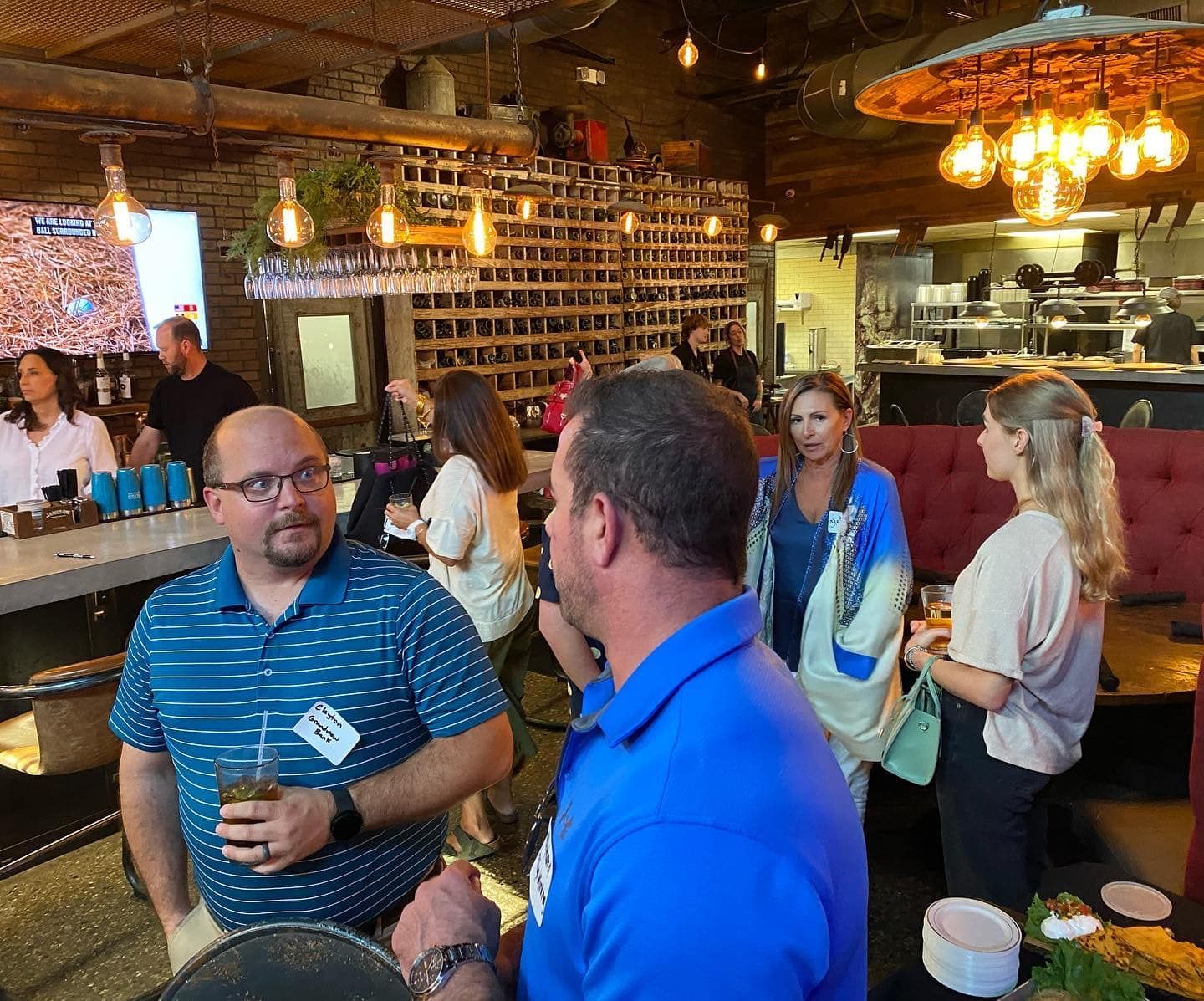 A group of people are standing in a restaurant talking to each other.