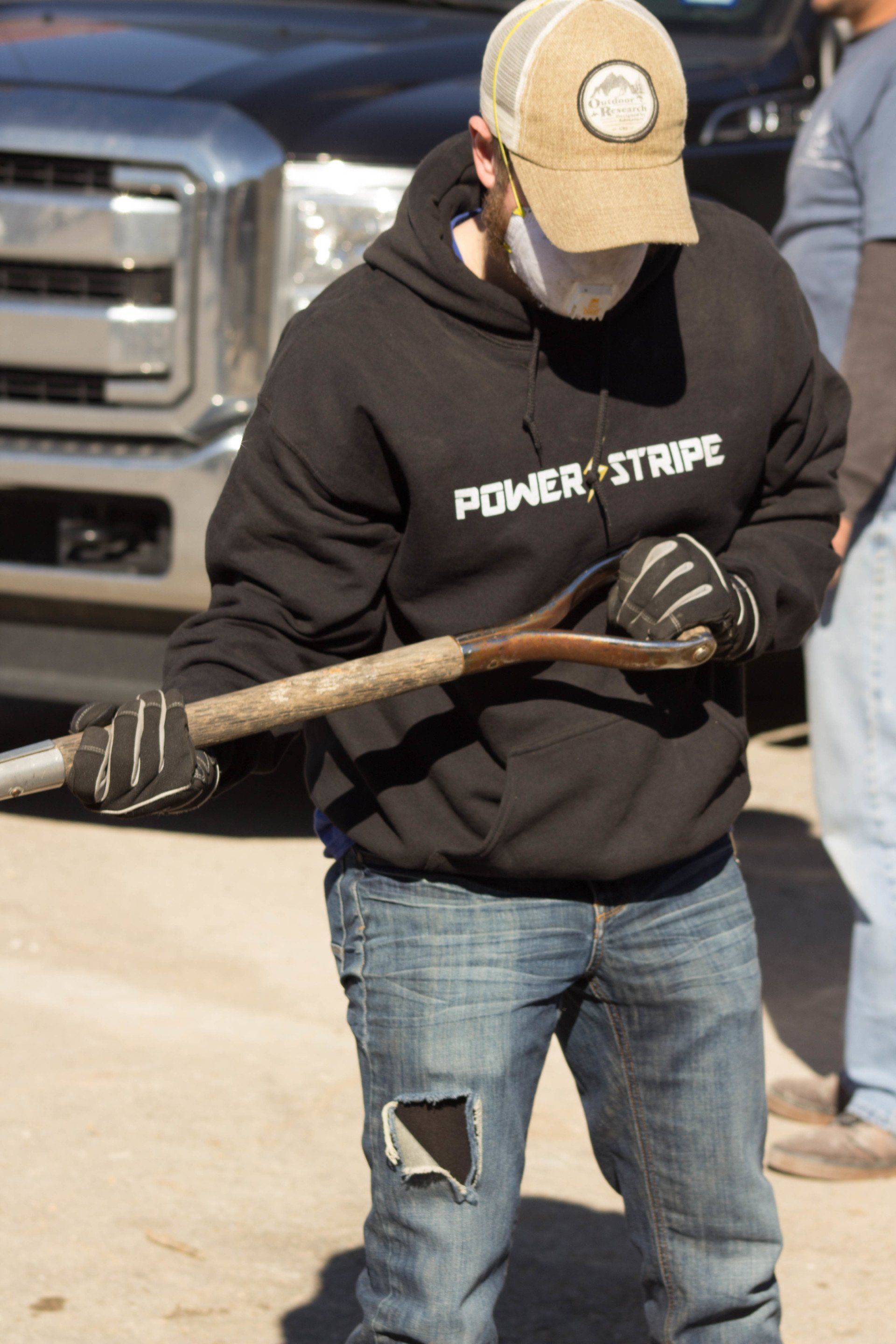A man wearing a power stripe sweatshirt is holding a wooden stick