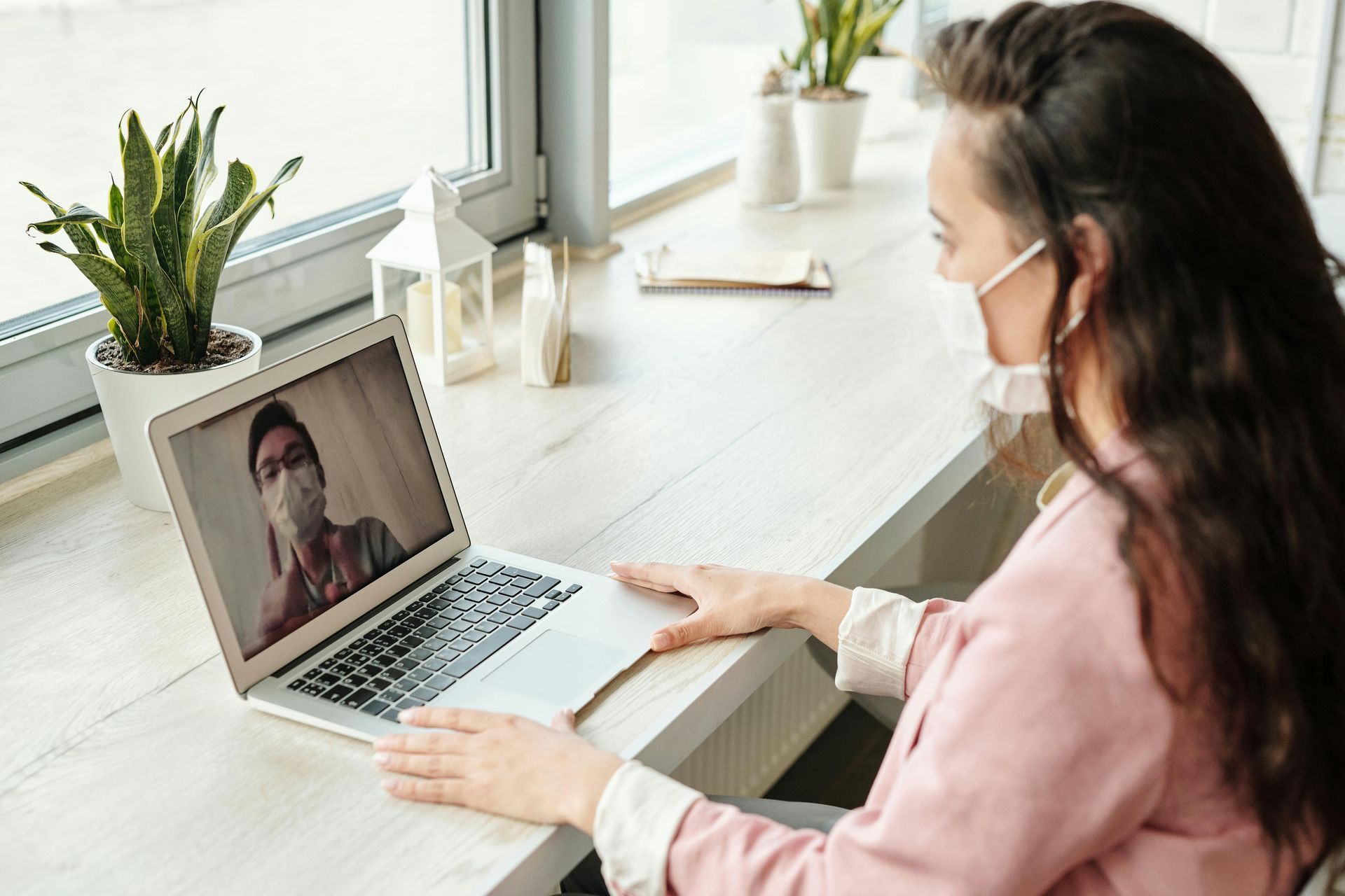 A woman wearing a mask is sitting at a desk using a laptop computer.