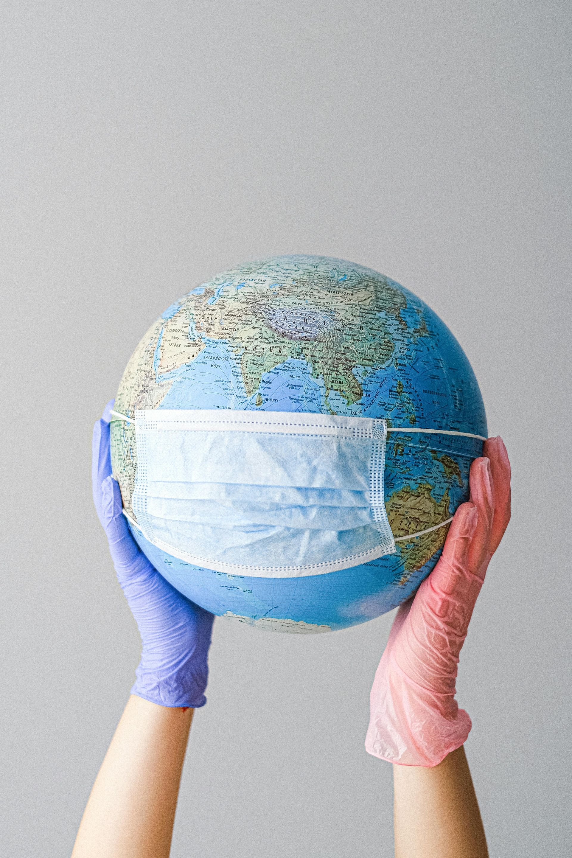 A person wearing gloves is holding a globe with a mask on it.