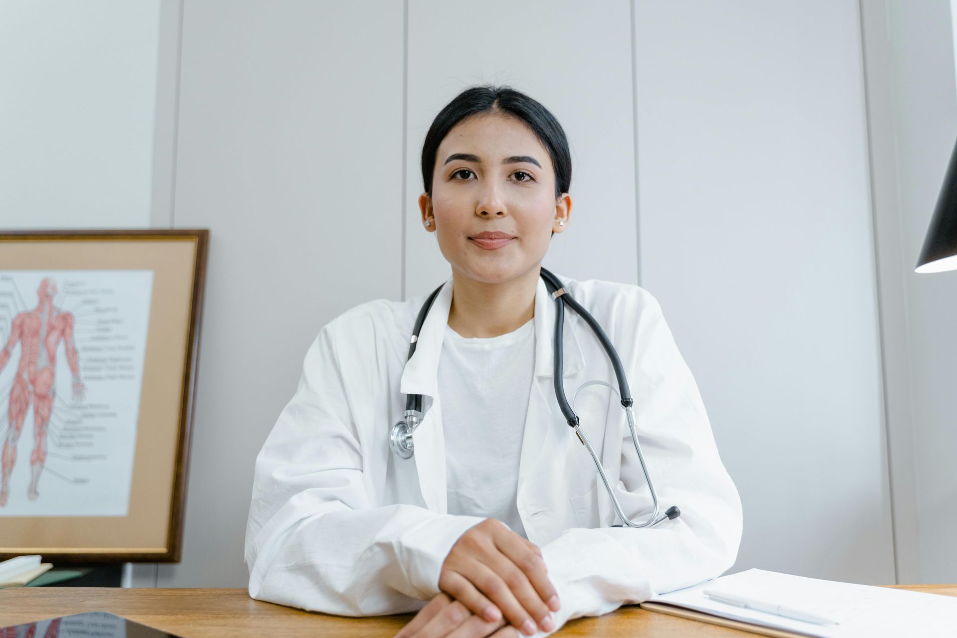 A female doctor is sitting at a desk with her hands folded.