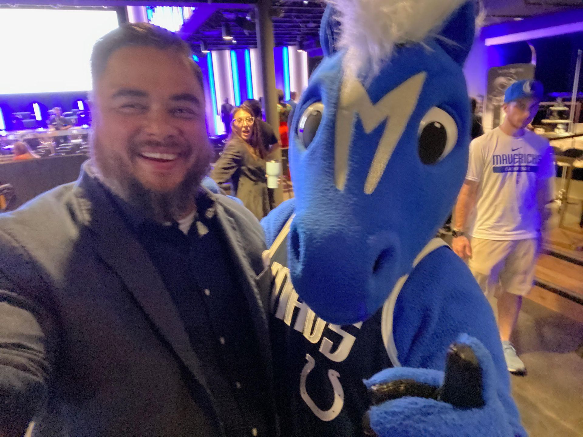 A man in a suit is standing next to a blue horse mascot